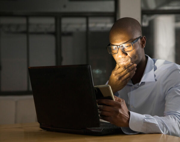 Mature black man while working on his laptop and mobile phone at night