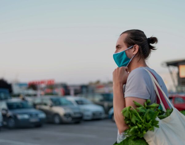 man in mask carrying a grocery bag in a car park